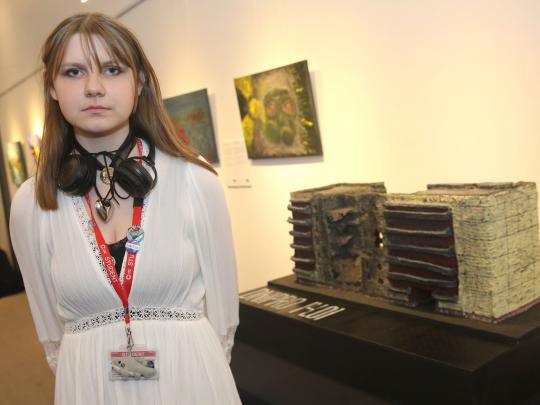 •	Uliana in front of her artwork, a model of a destroyed tower block in Dnipro.