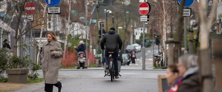 A cyclist on a road whilst a pedestrian crosses